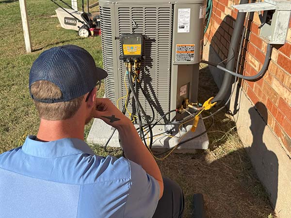 Air Conditioner technician sitting in front of unit ensuring maintenance